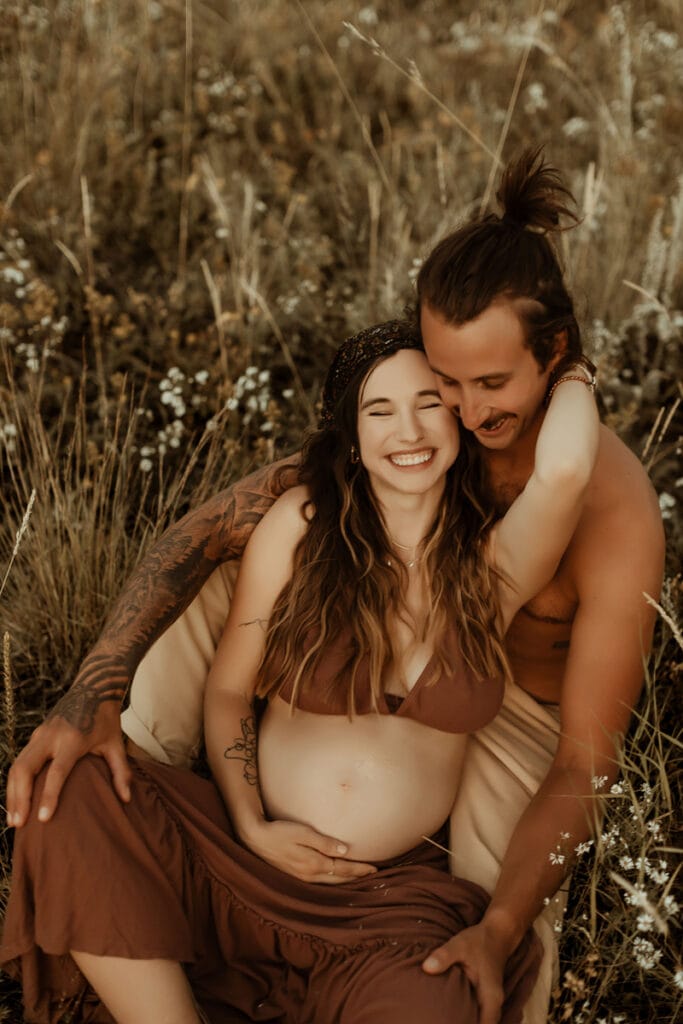 Maternity Photography, pregnant woman sitting in front of man holding her belly smiling