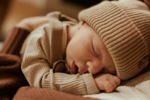 A newborn wearing a cozy hat sleeps on his mother's chest.
