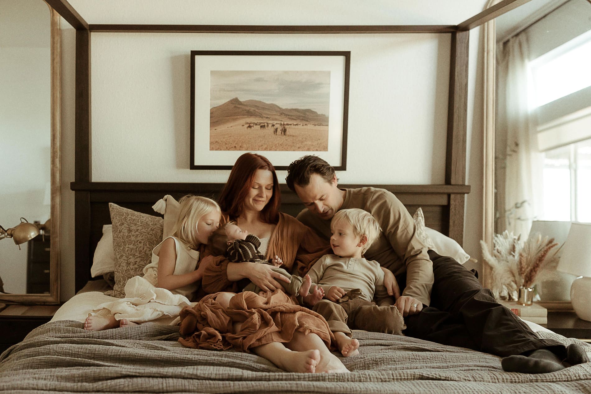 A family sits on a bed together and cuddles their newborn during an in-home newborn photoshoot in Denver, Colorado.